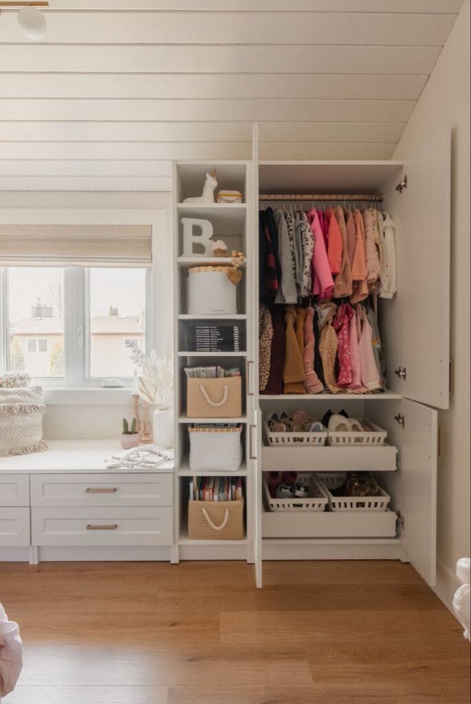 A well-organized closet with built-in shelves and drawers, neatly arranged with clothes, shoes, and storage baskets. A window with blinds provides natural light to the space, enhancing its brightness and functionality.