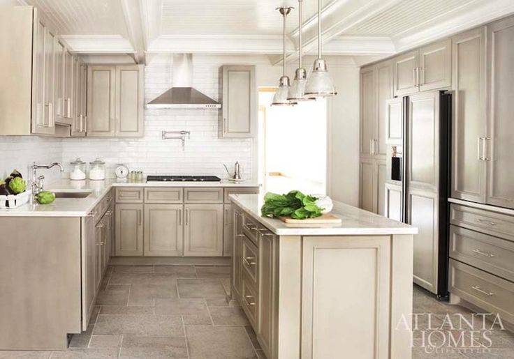 "Modern kitchen with neutral gray cabinets, stainless steel appliances, pendant lights, and a spacious island with green vegetables on the countertop"