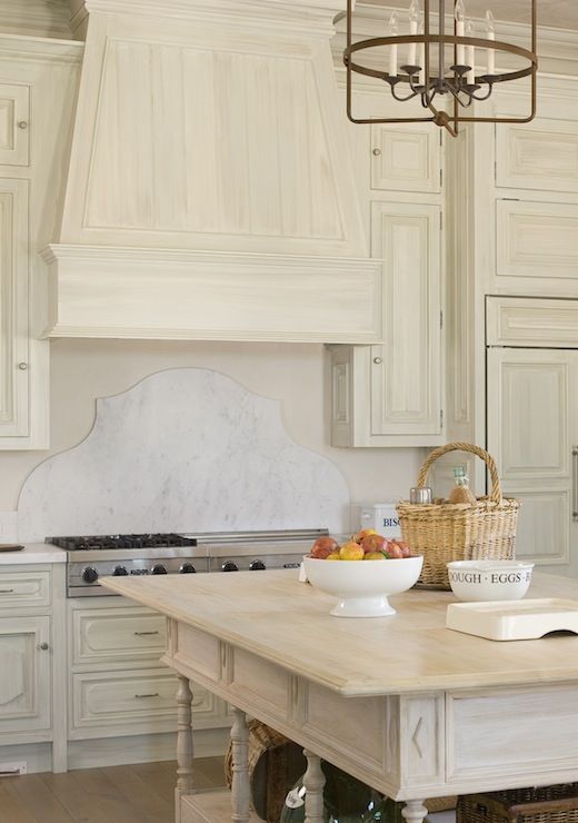 "Kitchen with white washed oak cabinets, marble countertops, and a wooden island with a fruit bowl on top"